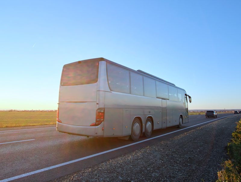 A silver motorcoach on an open highway at sunrise